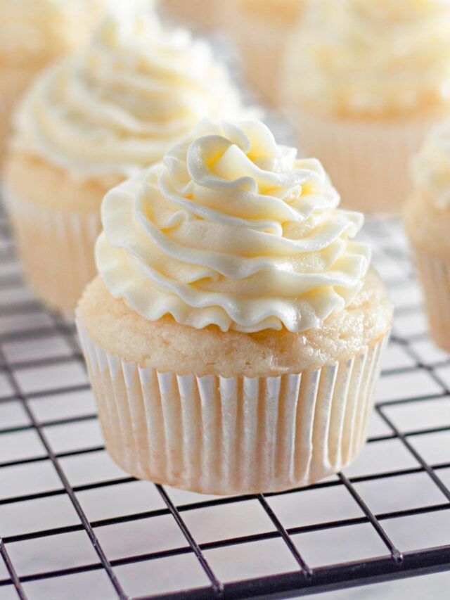 Buttercream Frosting piped onto vanilla cupcakes and left to cool on a cooling rack.