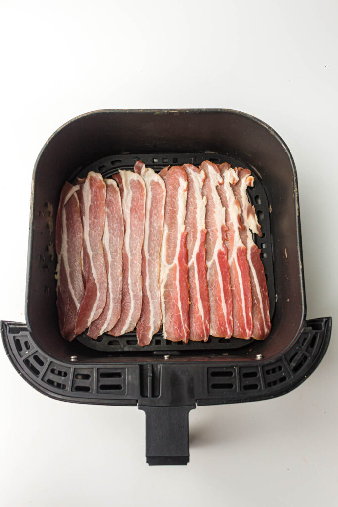 Raw bacon in the basket of an air fryer.