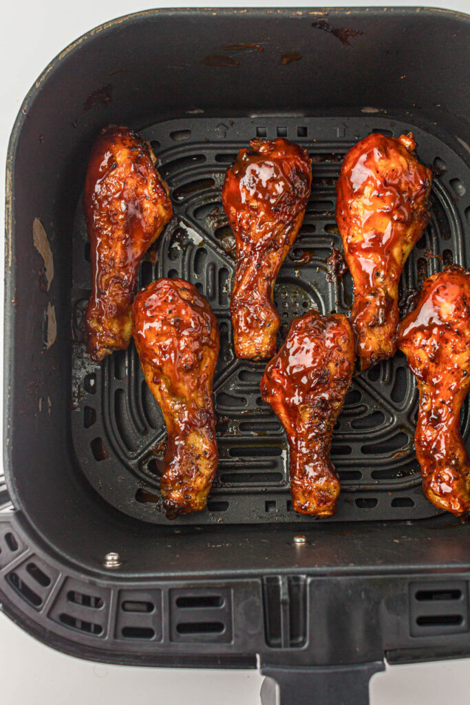 Chicken legs coated in barbecue sauce in the basket of an air fryer.