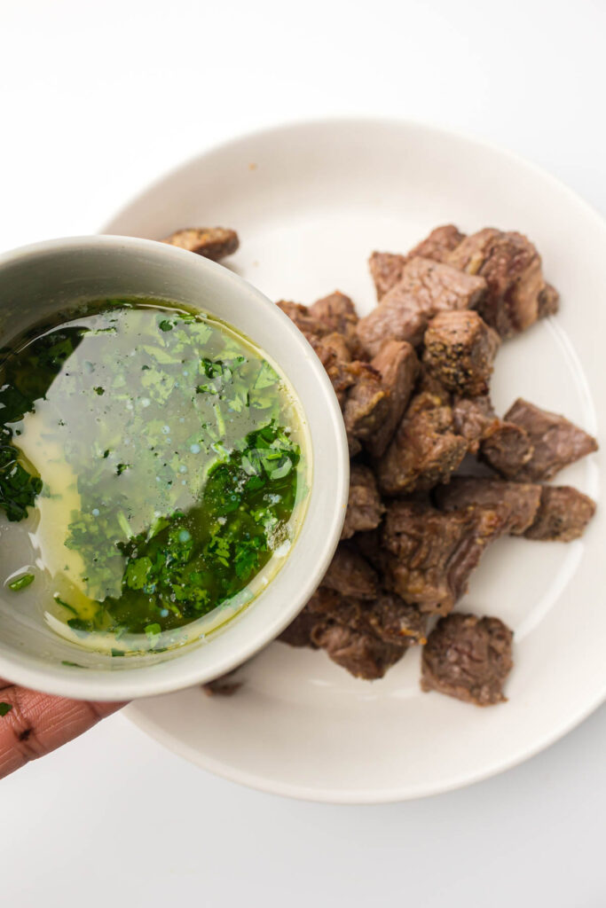 a hand pouring parsley butter over cooked steak.