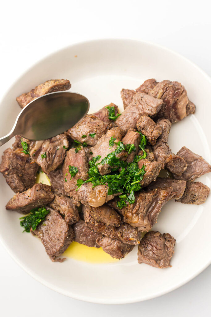 Air Fryer Steak Bites in a serving bowl topped with parsley.