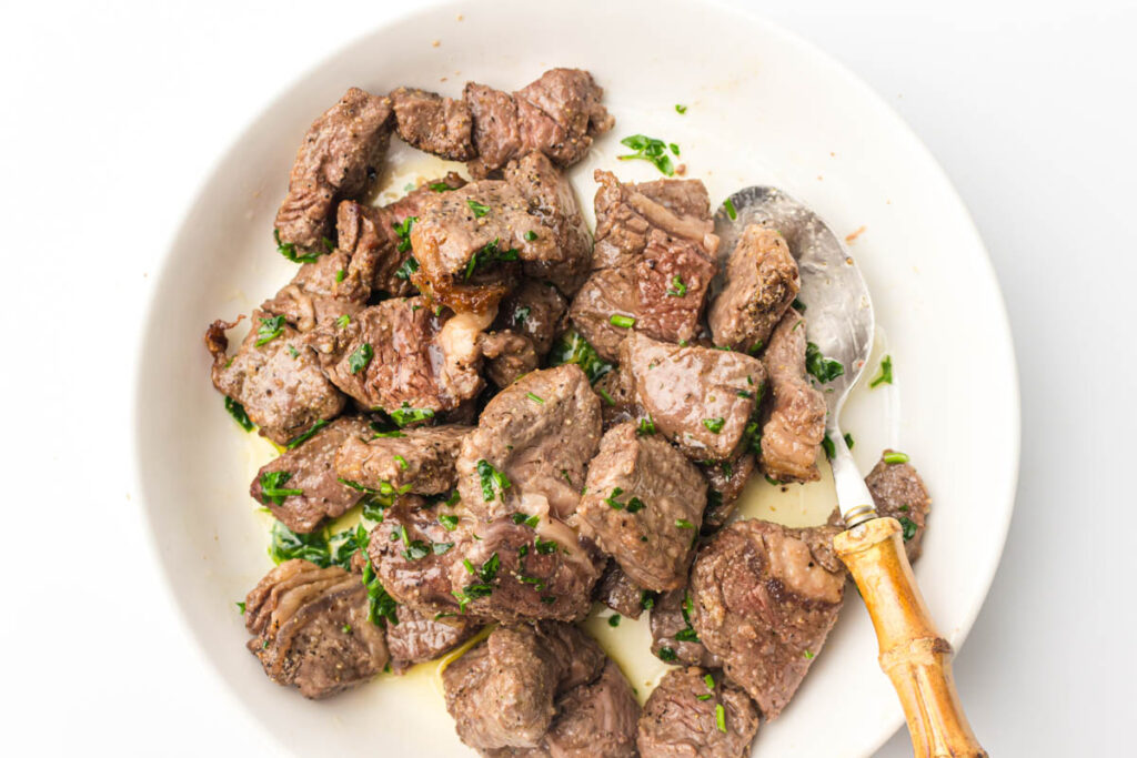 Garlic butter steak bites in a shallow bowl with a spoon.
