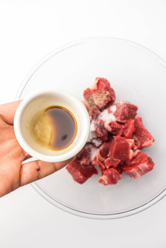 a glass bowl filled with steak, topped with soy sauce and seasonings