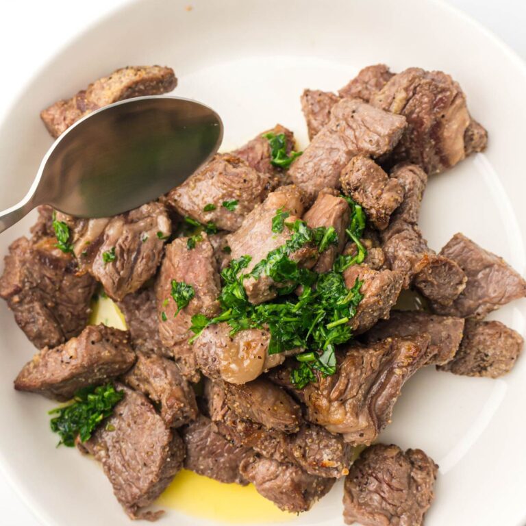 A bowl of air fryer steak bites drizzled with butter.