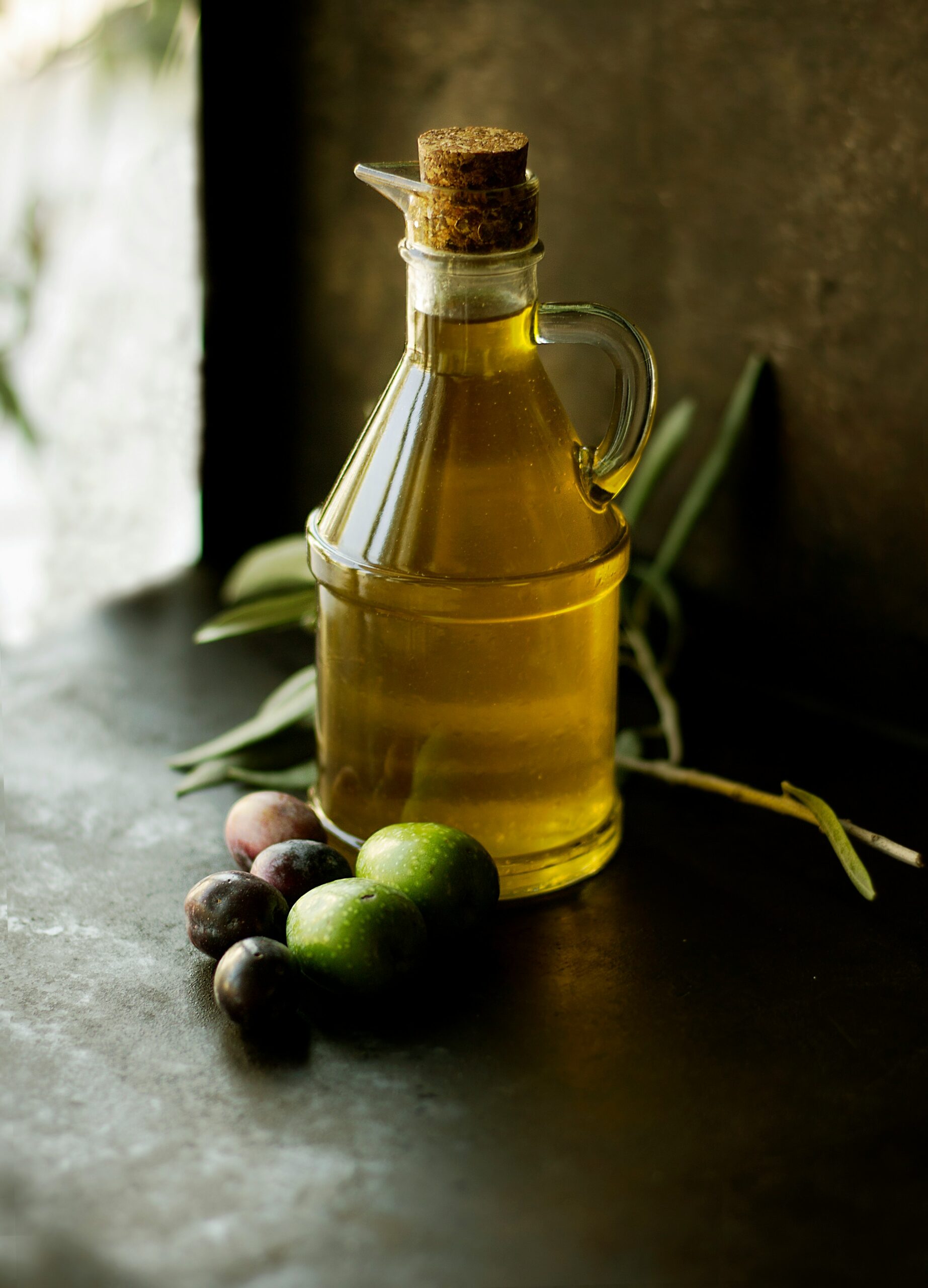 A bottle of olive oil with olives in front of it.