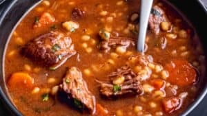 Close-up of a hearty beef soup with vegetables and beans in a black bowl.